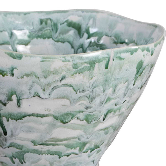 A sculptural ceramic vase with a wide, flared top and a narrow pedestal base, featuring a marbled, cloud-like pattern in sage green and white. It is photographed in a minimalist white corner studio setting with a soft shadow cast to the right.
