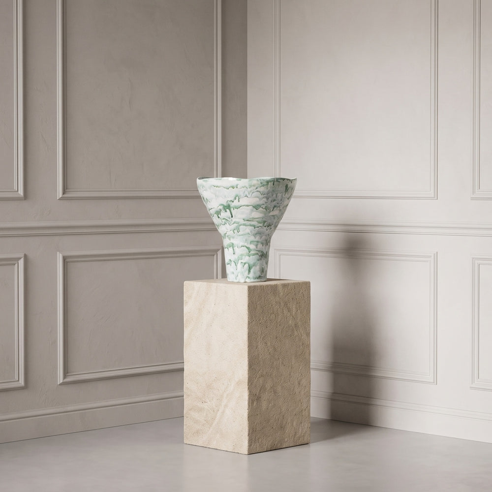 A green and white marbled ceramic vase displayed on a beige stone pedestal against a light gray paneled wall.