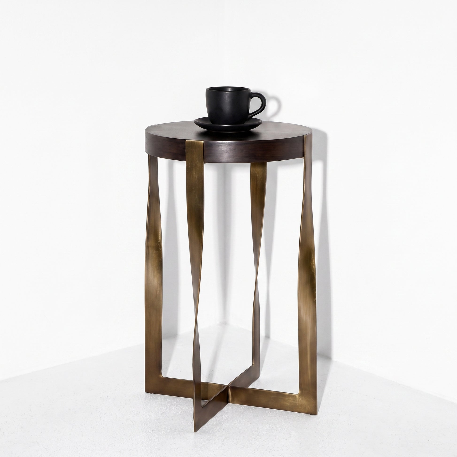 A modern round side table with a dark brown top and a bronze-finished twisted metal frame base, shown on a white background with a black coffee cup on top.