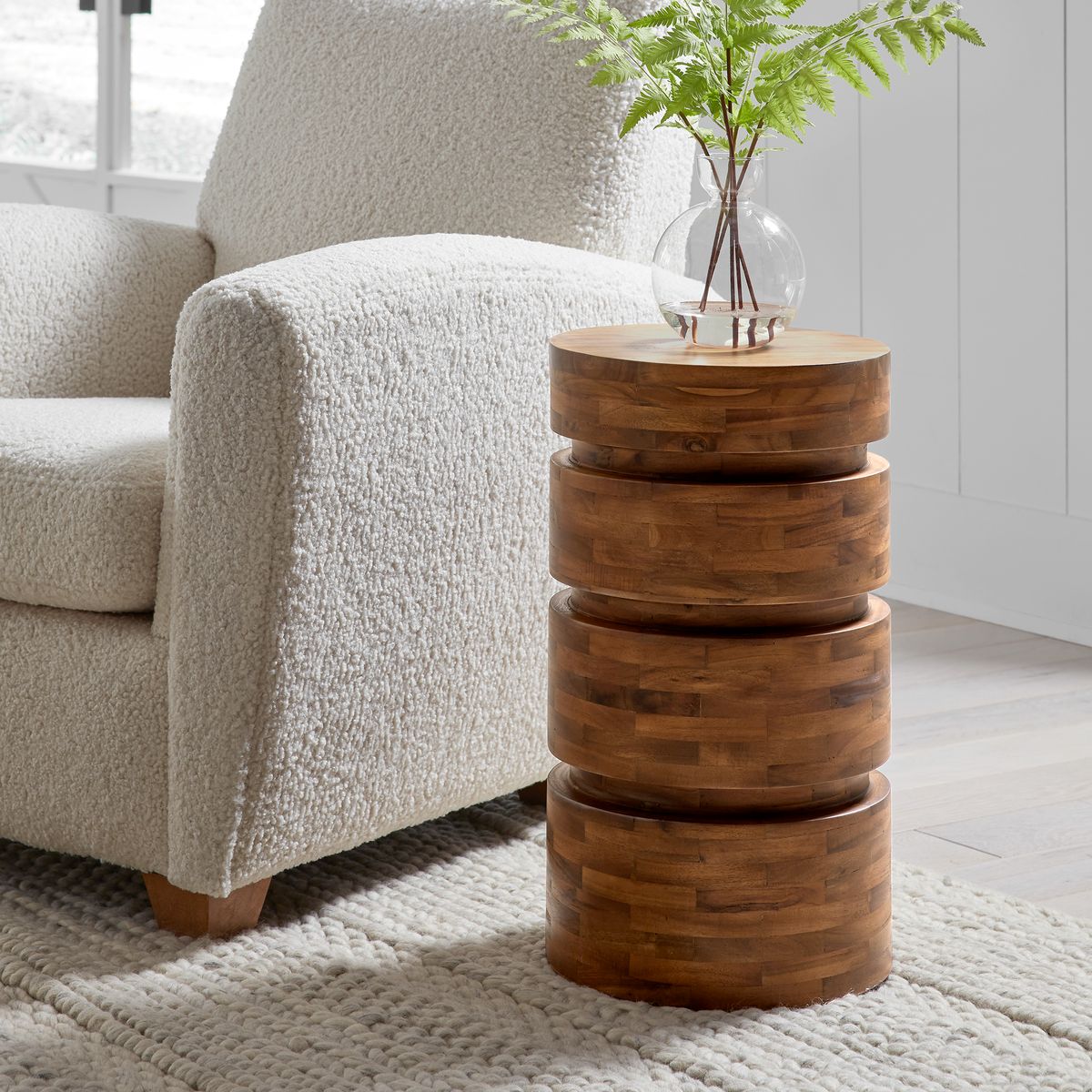 Wood accent table next to boucle armchair with plant on top.