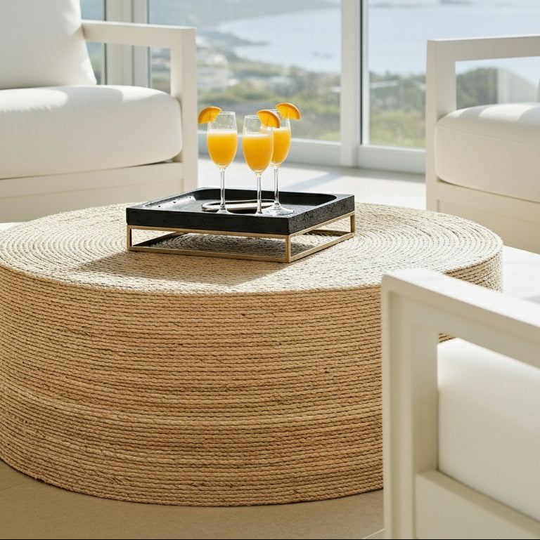 Modern living room with white chairs, a round woven coffee table, and large windows with a scenic view.