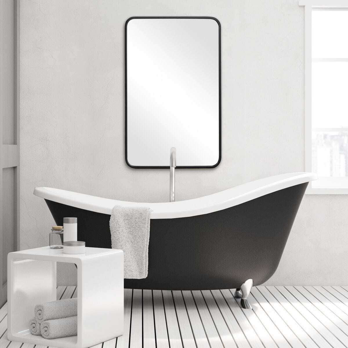 Modern bathroom with a black freestanding bathtub, white towels, and a mirror.