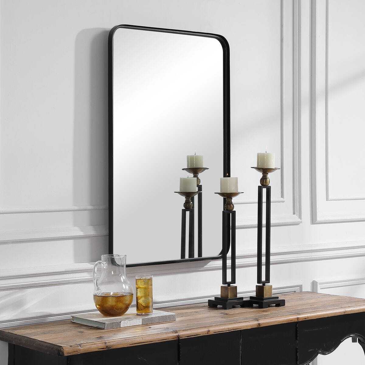 Decorative mirror with candle holders on a wooden console table against a white wall.