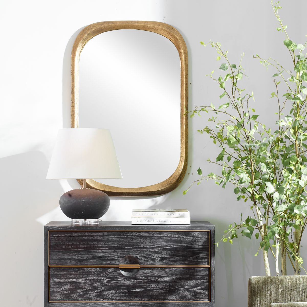 Nighstand with lamp, mirror, and plant against a light gray wall
