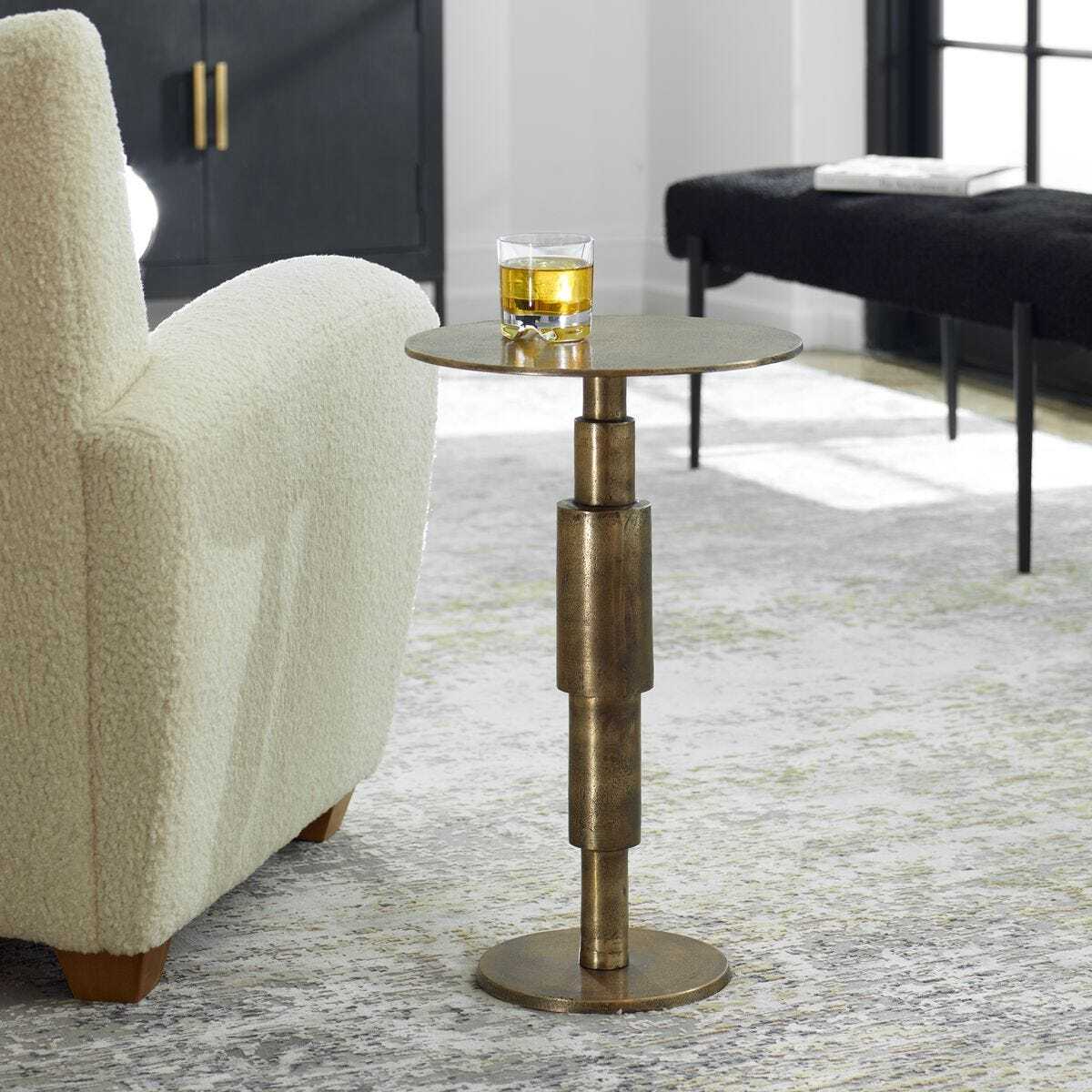 Bronze side table with a glass of yellow liquid in a living room setting