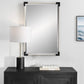 Nautical Mirror with White Rope frame and black corners over hanging a wood black console with a table lamp and white decorative books. An ocean photo hangs beside the mirror.