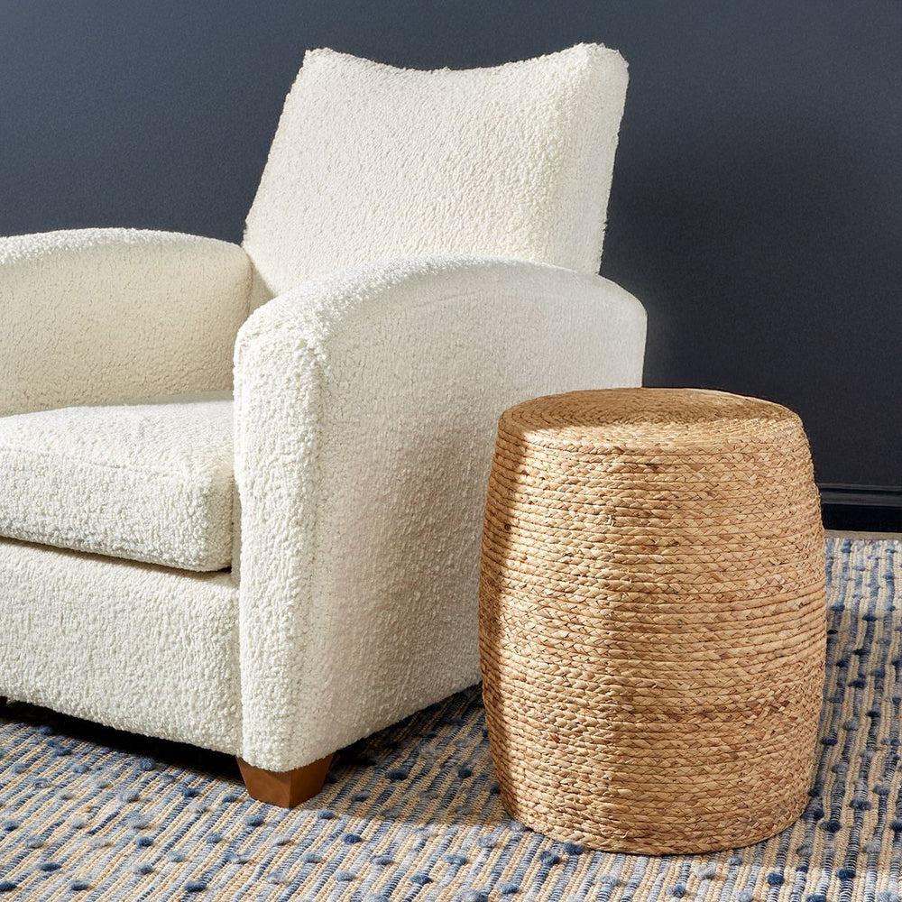 Woven straw round side table next to a boucle chair in a navy room.