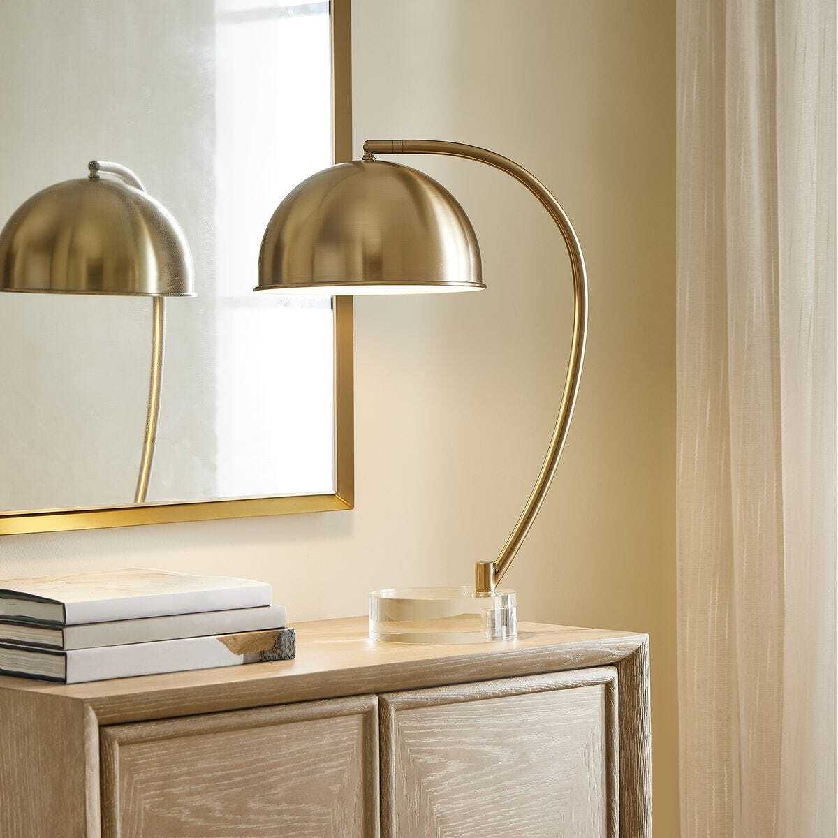 Gold table lamp on a wooden sideboard with a mirror in the background