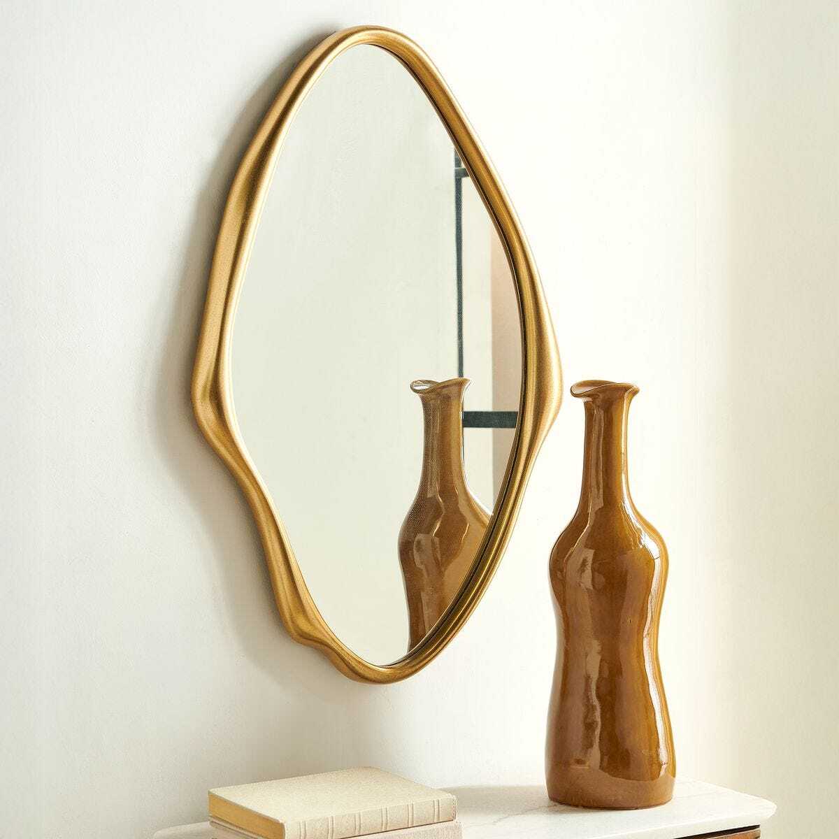 Gold-framed mirror and brown vase on a white surface with a white wall background