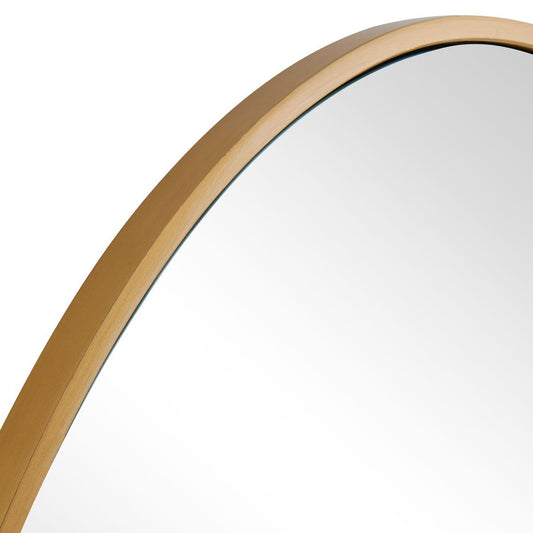 Round mirror on a wall with a lamp on a small table in a room with arched windows.