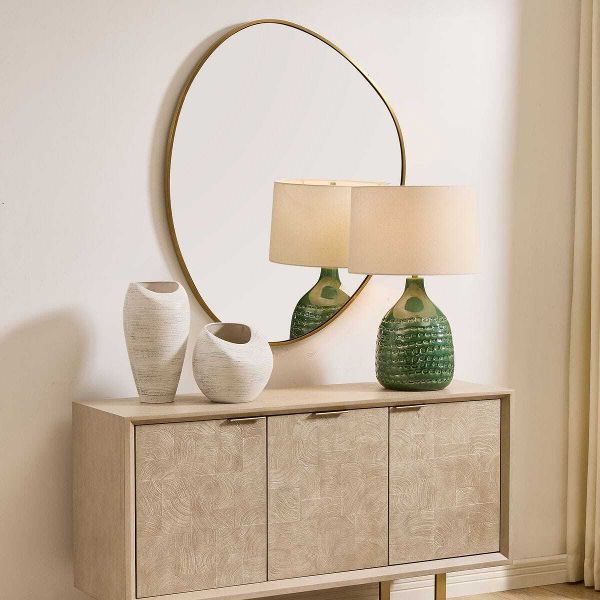 Beige sideboard with decorative items including a round mirror, lamps, and vases against a light wall.