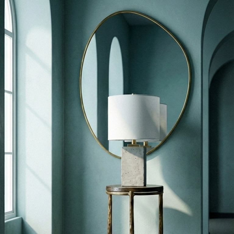 Round mirror on a wall with a lamp on a small table in a room with arched windows.