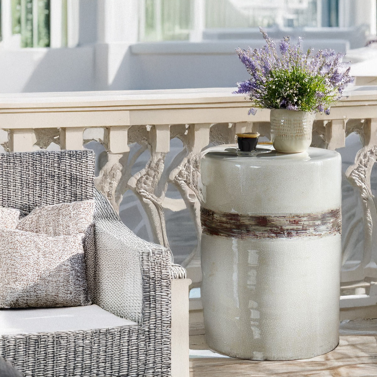 Outdoor white ceramic table with lavender on top and a coffee. Next to an outdoor wicker chair.