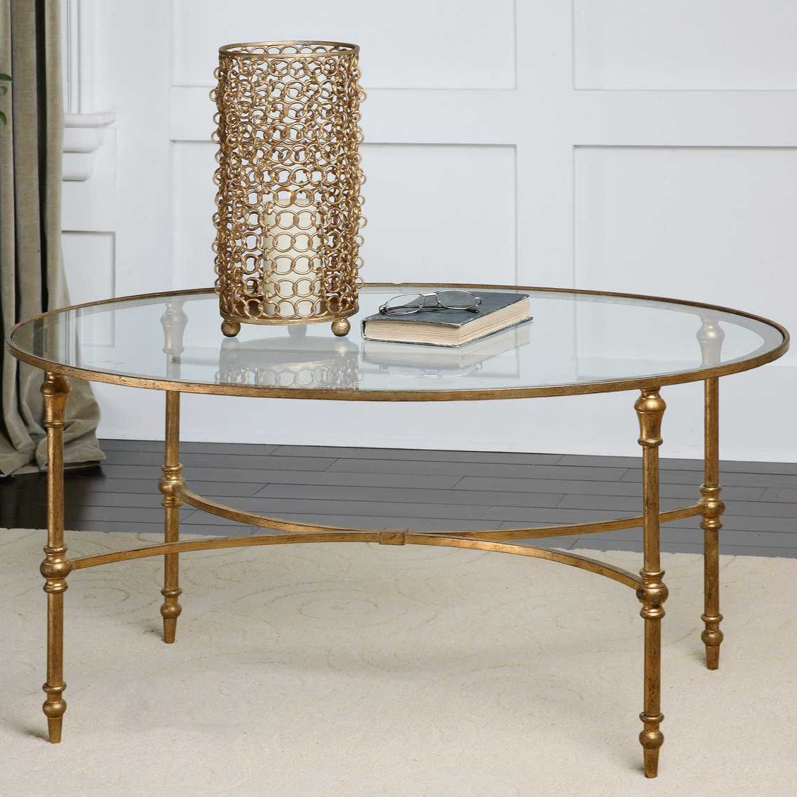 Gold round coffee table with glass top and decorative lamp in a room setting.