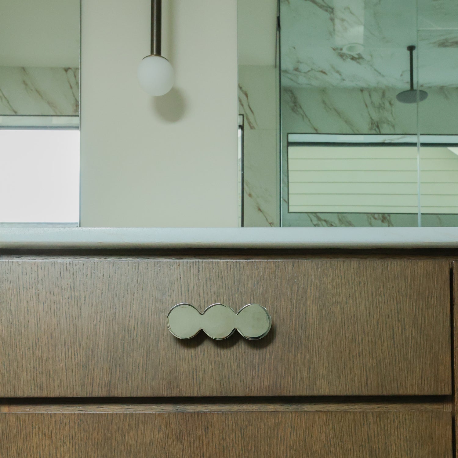 Statement circular cabinet pull in polished nickel mounted on a bathroom cabinet.