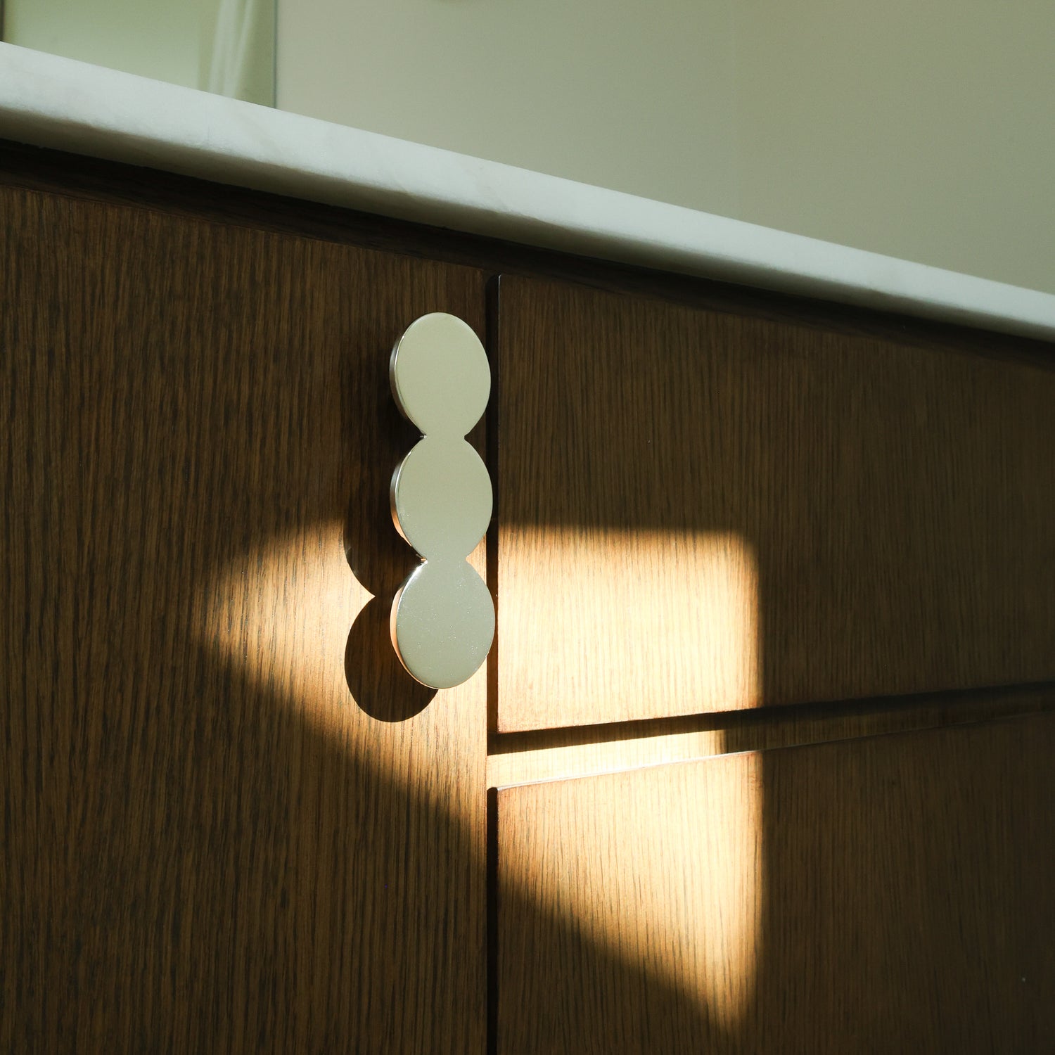 Statement circular cabinet pull in polished nickel mounted on a bathroom cabinet.