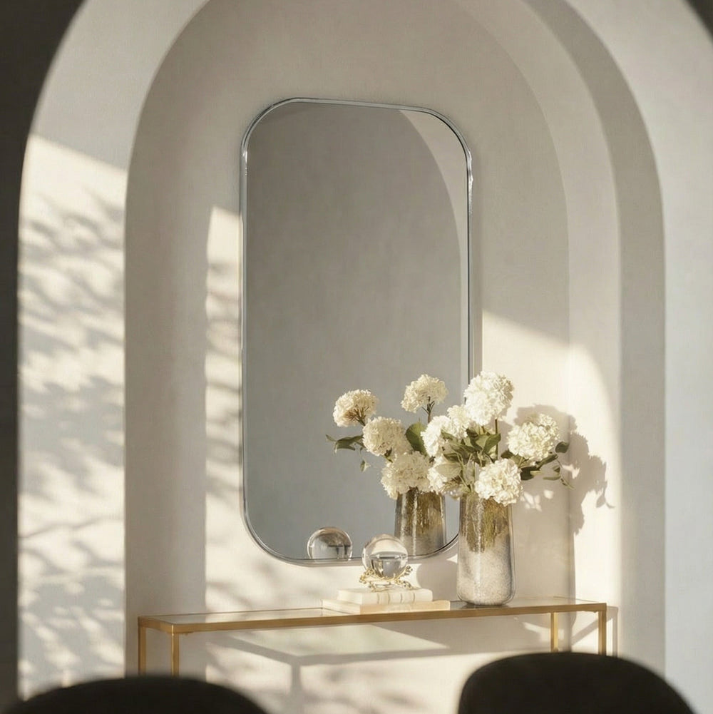 Decorative setup with a polished nickel framed mirror, flowers, and a vase in a softly lit room.