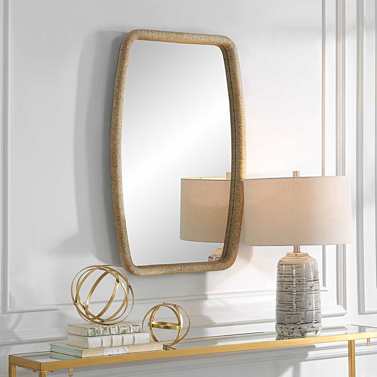 Decorative mirror with gold frame on a wall above a console table with lamps and decorative items.