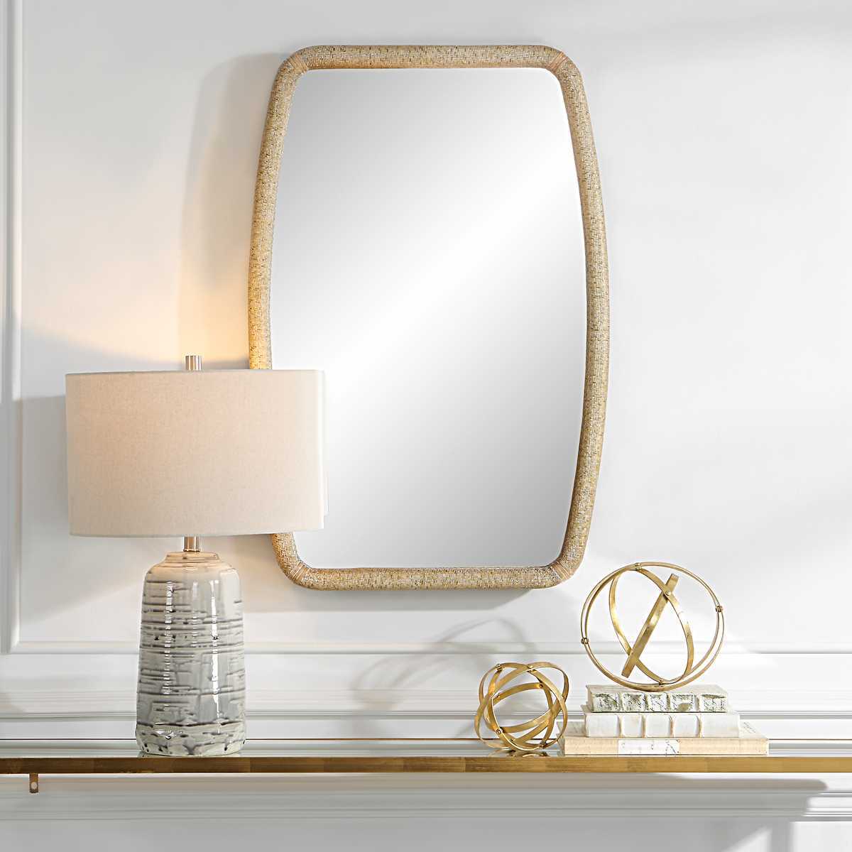 Decorative mirror with gold frame on a shelf with a lamp and small decorative items.