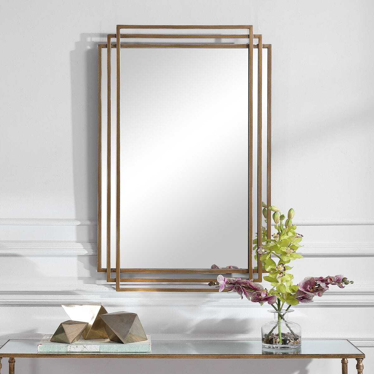 Decorative mirror with gold frame on a white wall above a console table with decorative items.
