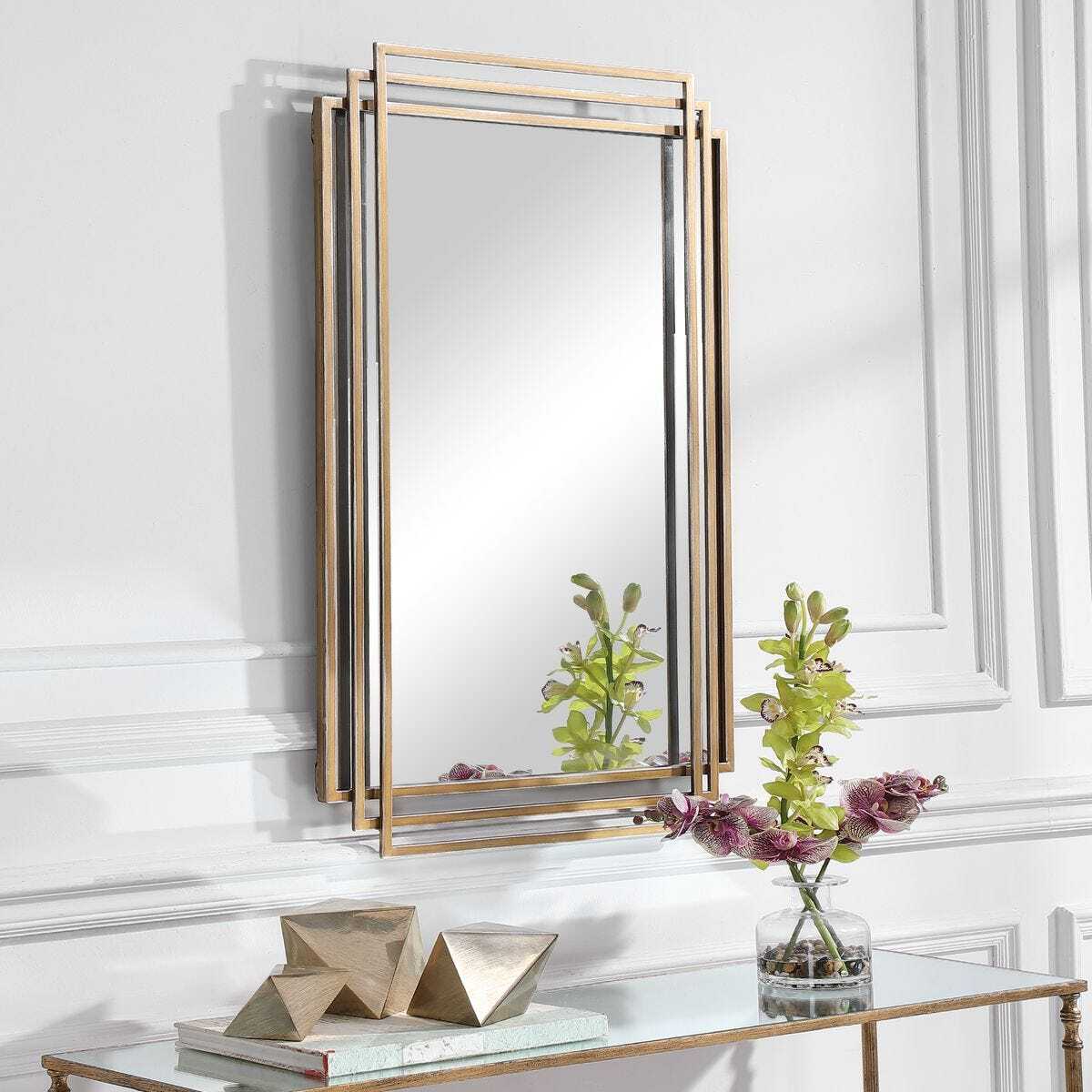 Gold-framed mirror on a white wall with decorative elements below.