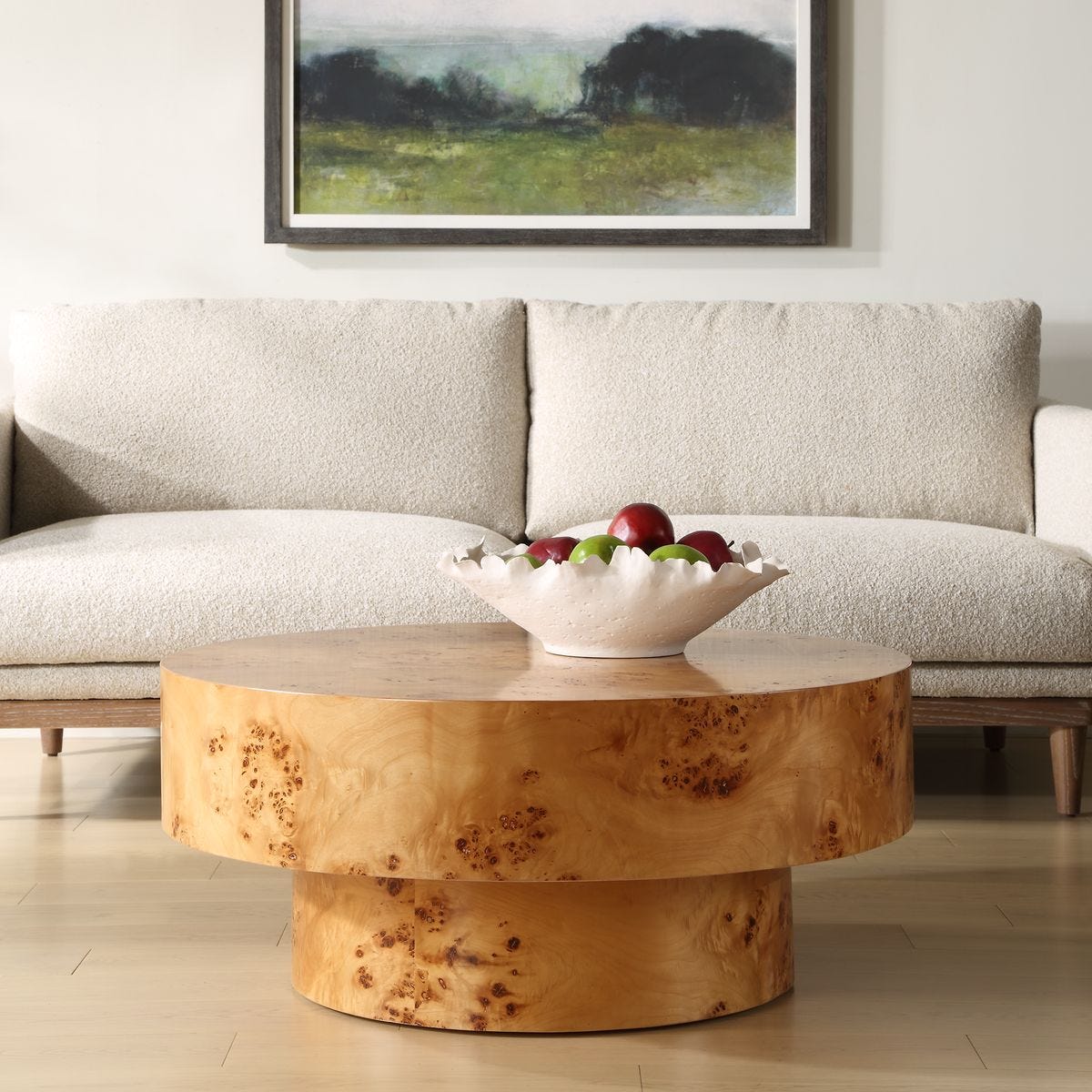 Wooden coffee table with a bowl of fruit in front of a beige sofa and framed artwork.
