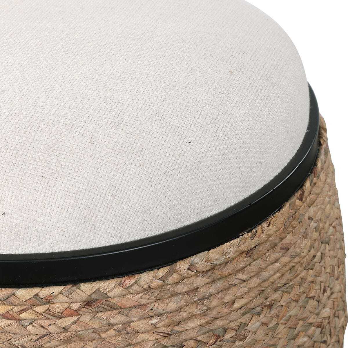 Close-up of a woven natural-fiber stool or ottoman with a light beige fabric cushion and a black rim.