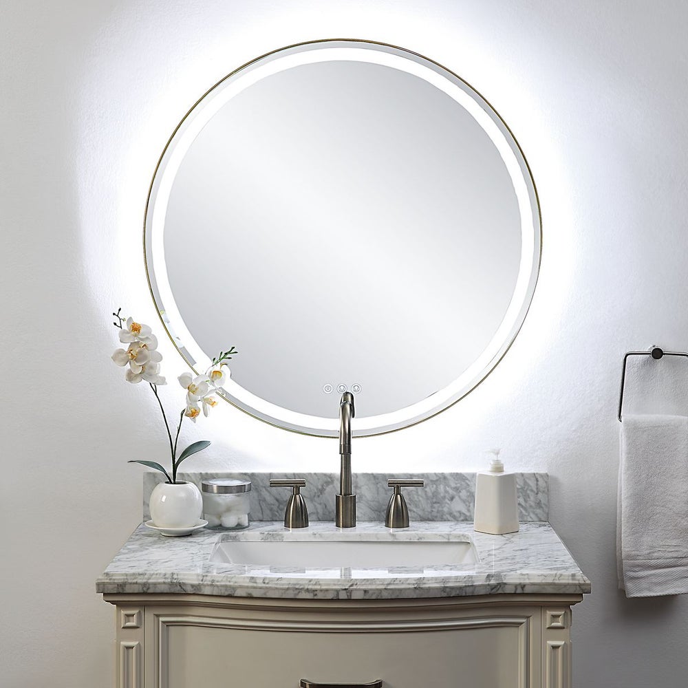 Lighted round gold mirror above marble vanity.