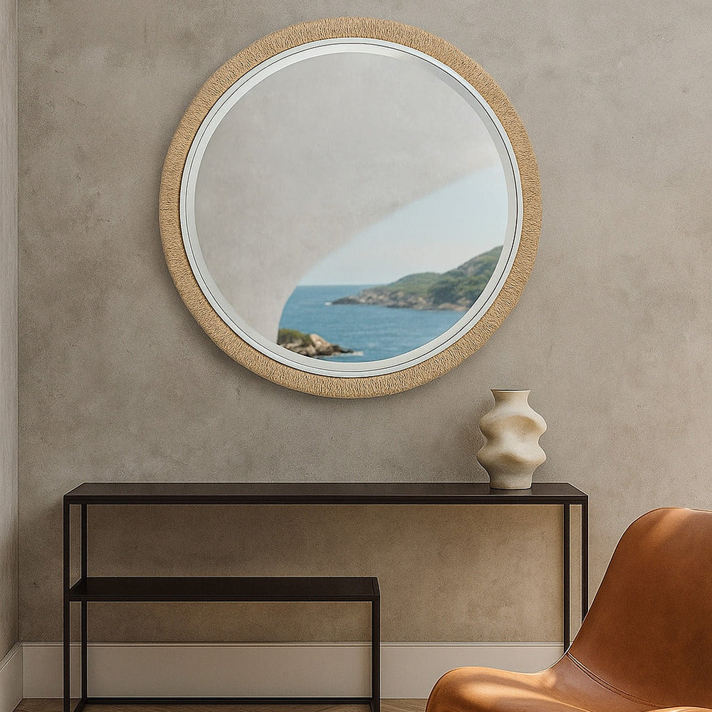 Round mirror with wooden frame on a beige wall above a black console table with a vase and a brown chair.