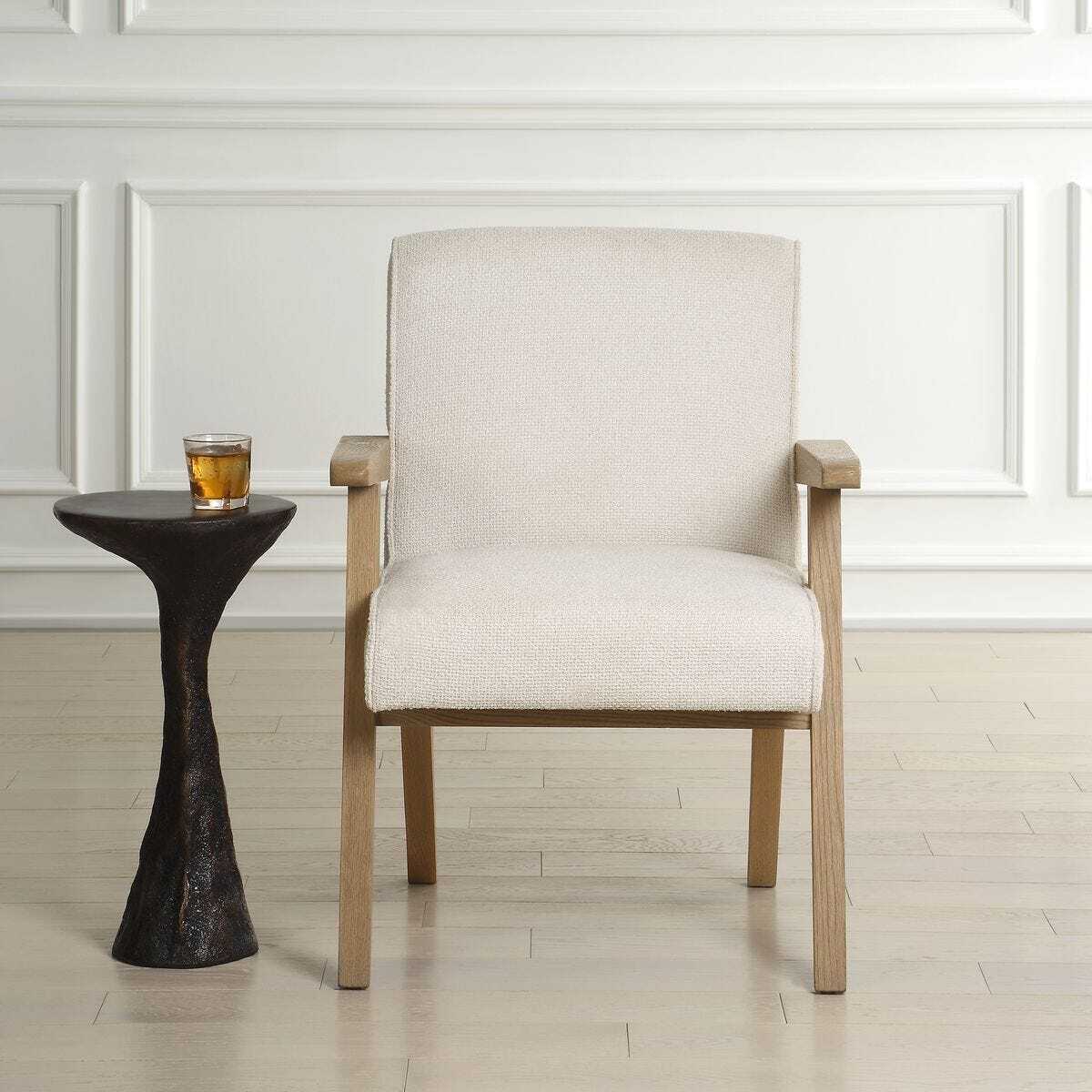 Beige armchair next to a small black side table with a glass on a wooden floor.