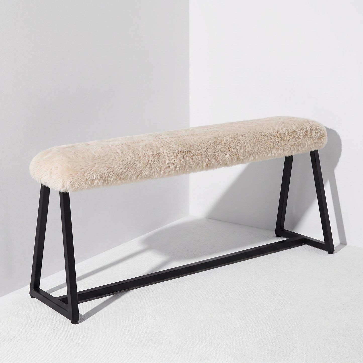 A modern bench with a cream-colored sheepskin or faux fur upholstered seat and a black metal frame, shown in a minimalist white studio setting.