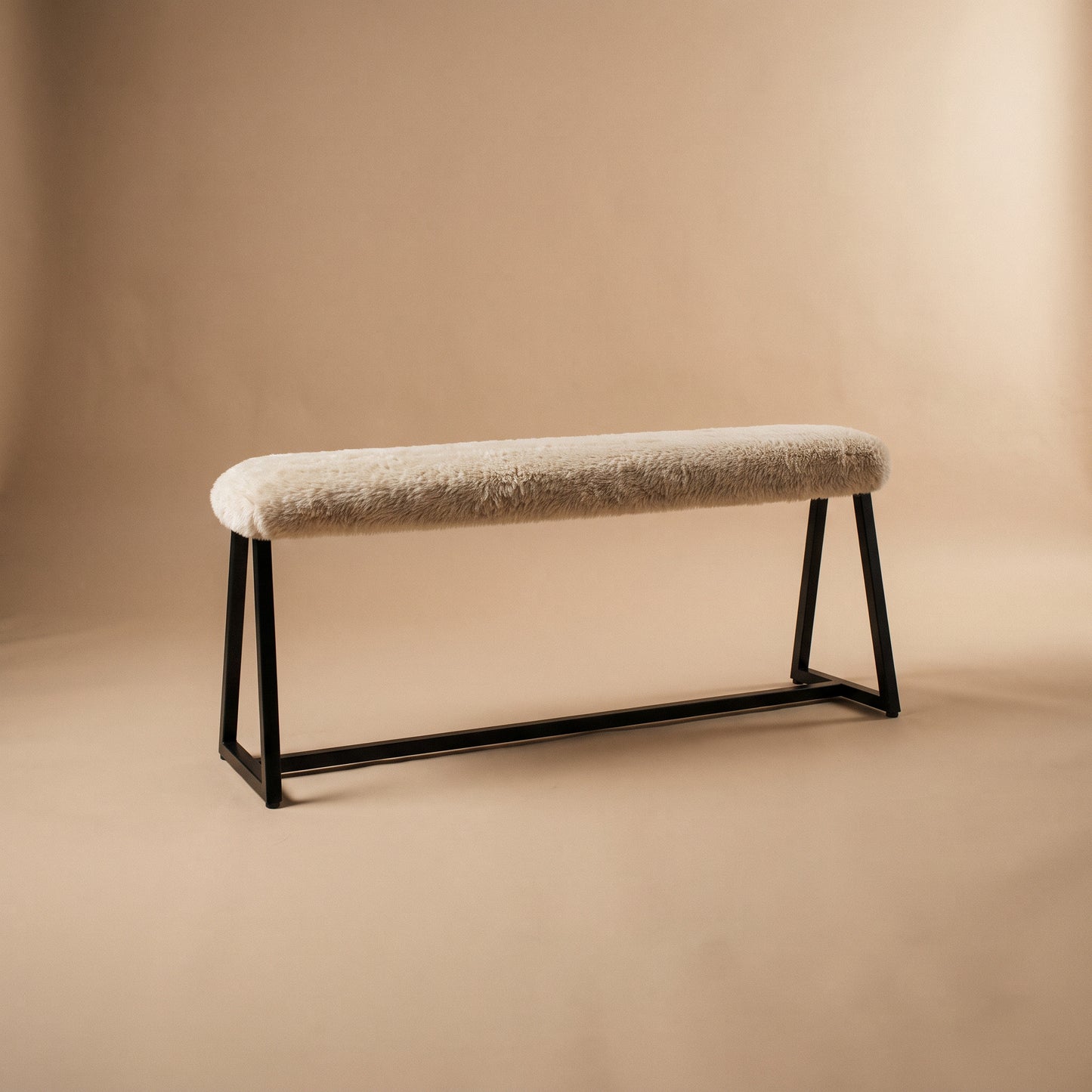 A modern bench with a textured cream bouclé seat cushion and a black metal frame, set against a warm beige studio background.