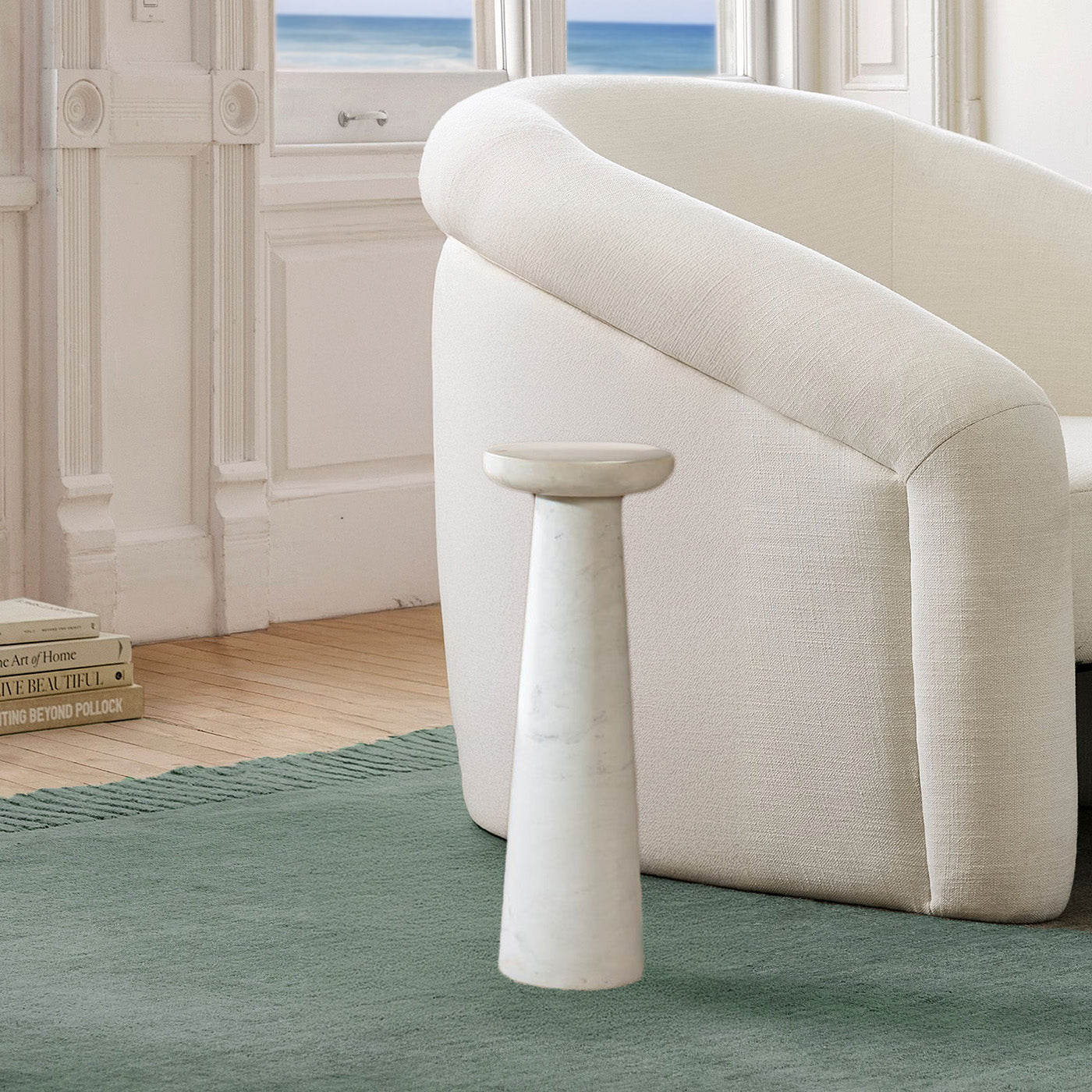 Small white marble drink table next to decorative chair in a coastal living room with an ocean view and a teal rug.