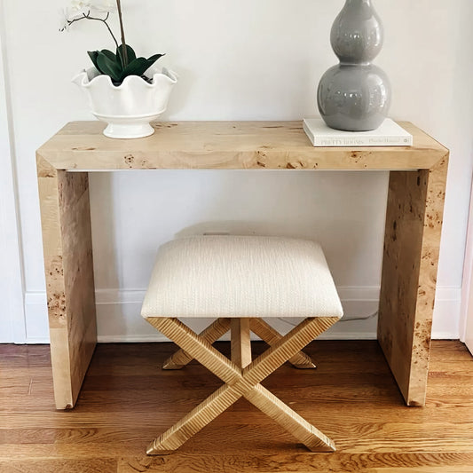 Console with decorative book and lamp with a woven rattan seat underneath in an entryway.