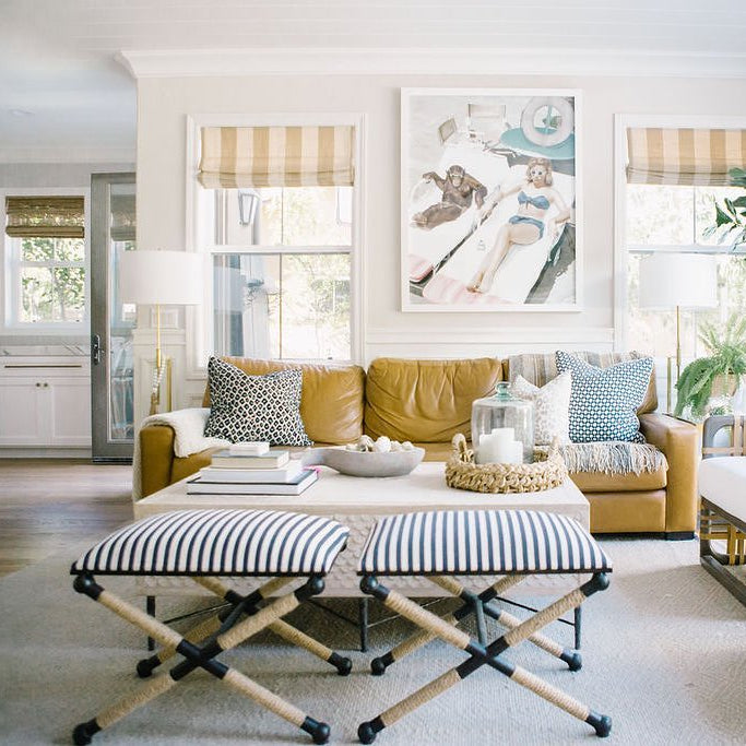 Modern living room with yellow sofa, striped ottomans, and decorative pillows.