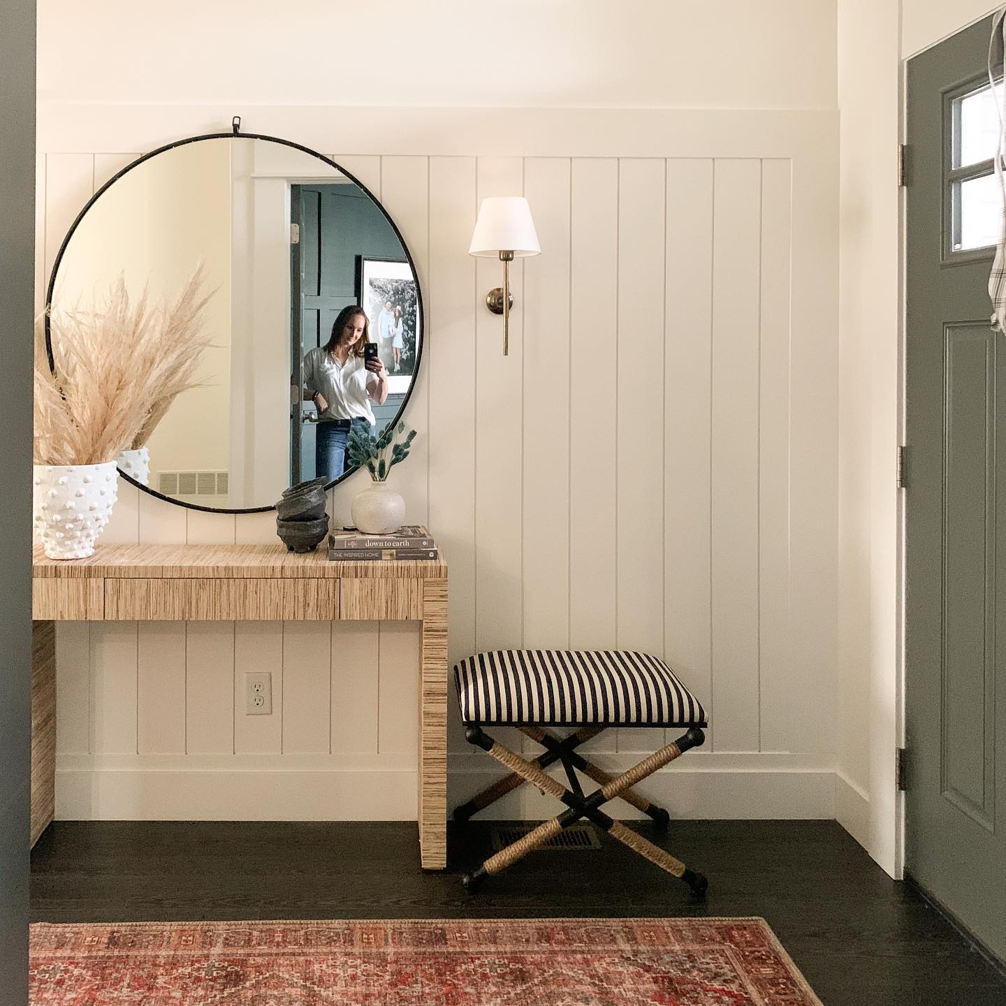 Dresser with round mirror, striped stool, and decorative items in a home setting.