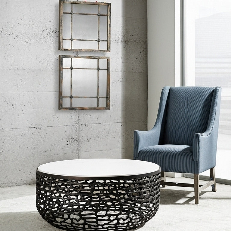 Modern living room with a blue armchair, round black coffee table, and wall mirrors.