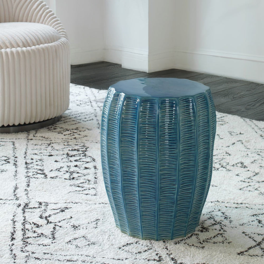 Teal garden stool in living room on chic white carpet with decorative chair