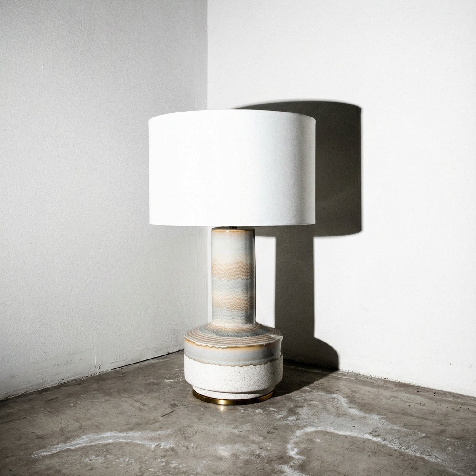 Table lamp with a white shade on a textured concrete floor against a gray wall.