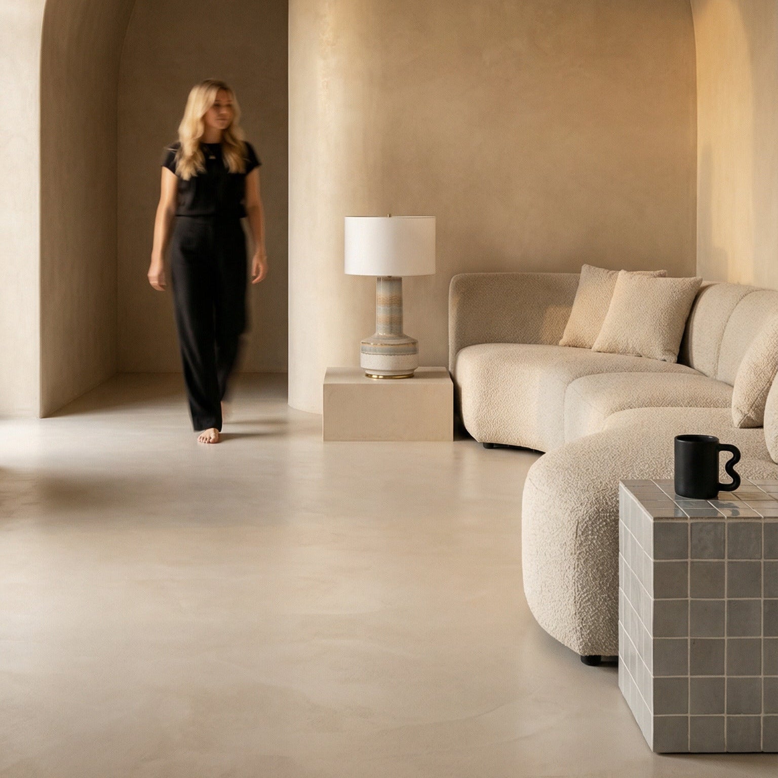Woman walking through a modern, arched hallway with a couch and lamp in the background.