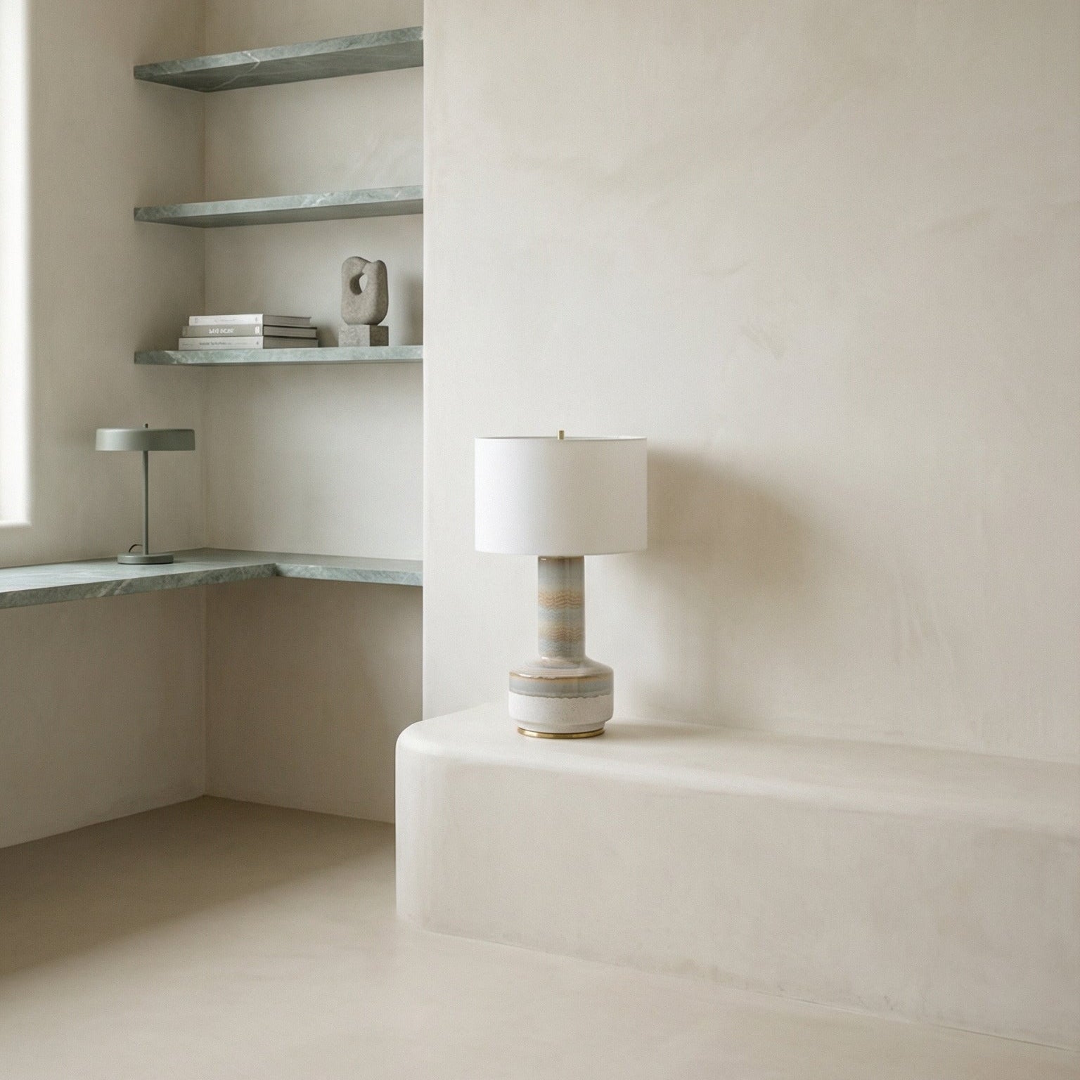 Minimalist interior with a lamp on a white surface and shelves against a beige wall.