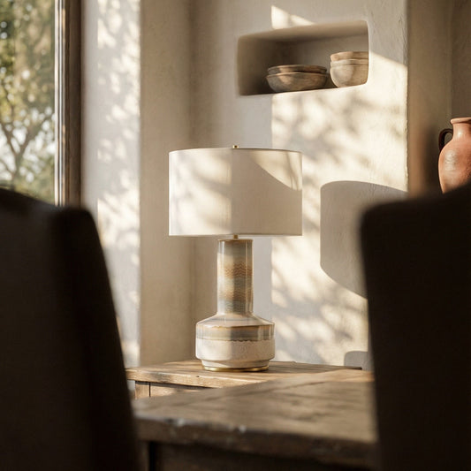 Table lamp with a white shade on a textured concrete floor against a gray wall.