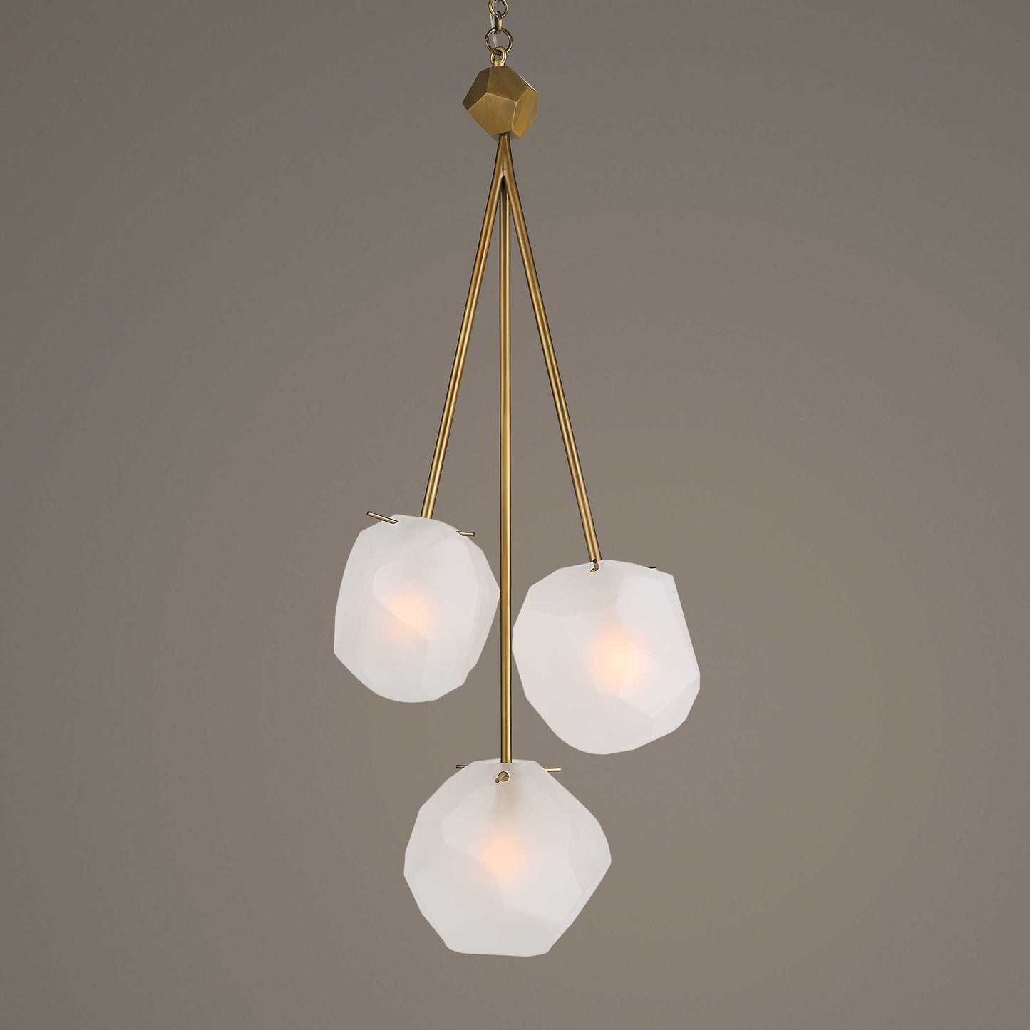 A three-light pendant light fixture with frosted glass shades and a matte antique brass finish.