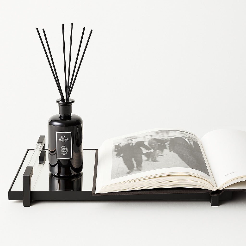 Black diffuser bottle on a black tray with an open book featuring black and white photos on a white background