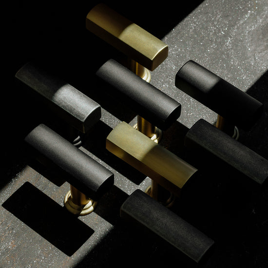 Two-tone solid brass knobs on a concrete background in satin brass, matte black, and unlacquered brass finishes.