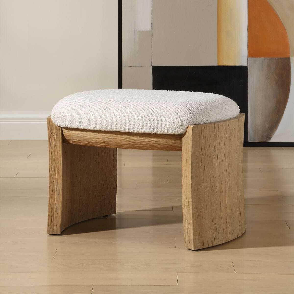 Wooden stool with a white cushioned seat in a room with abstract art on the wall.