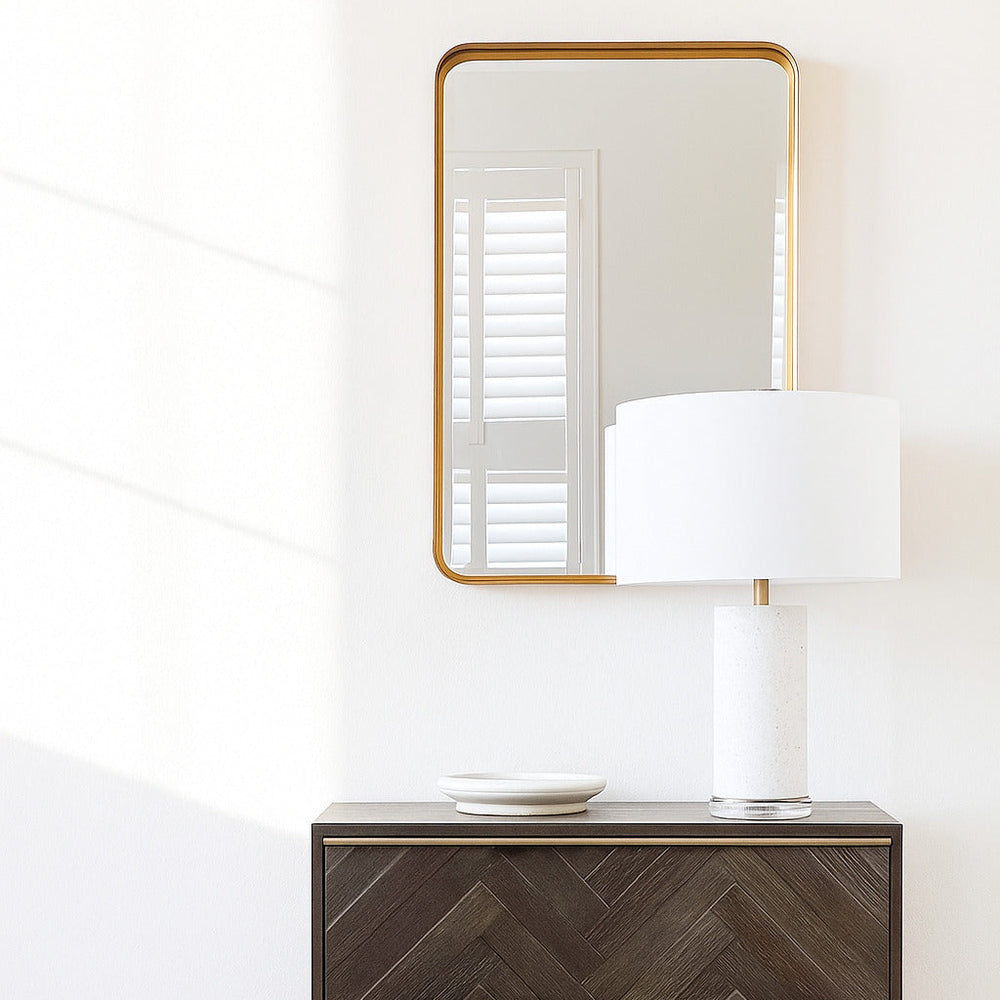 Wooden dresser with chevron pattern and gold frame, mirror above, white lamp on surface.