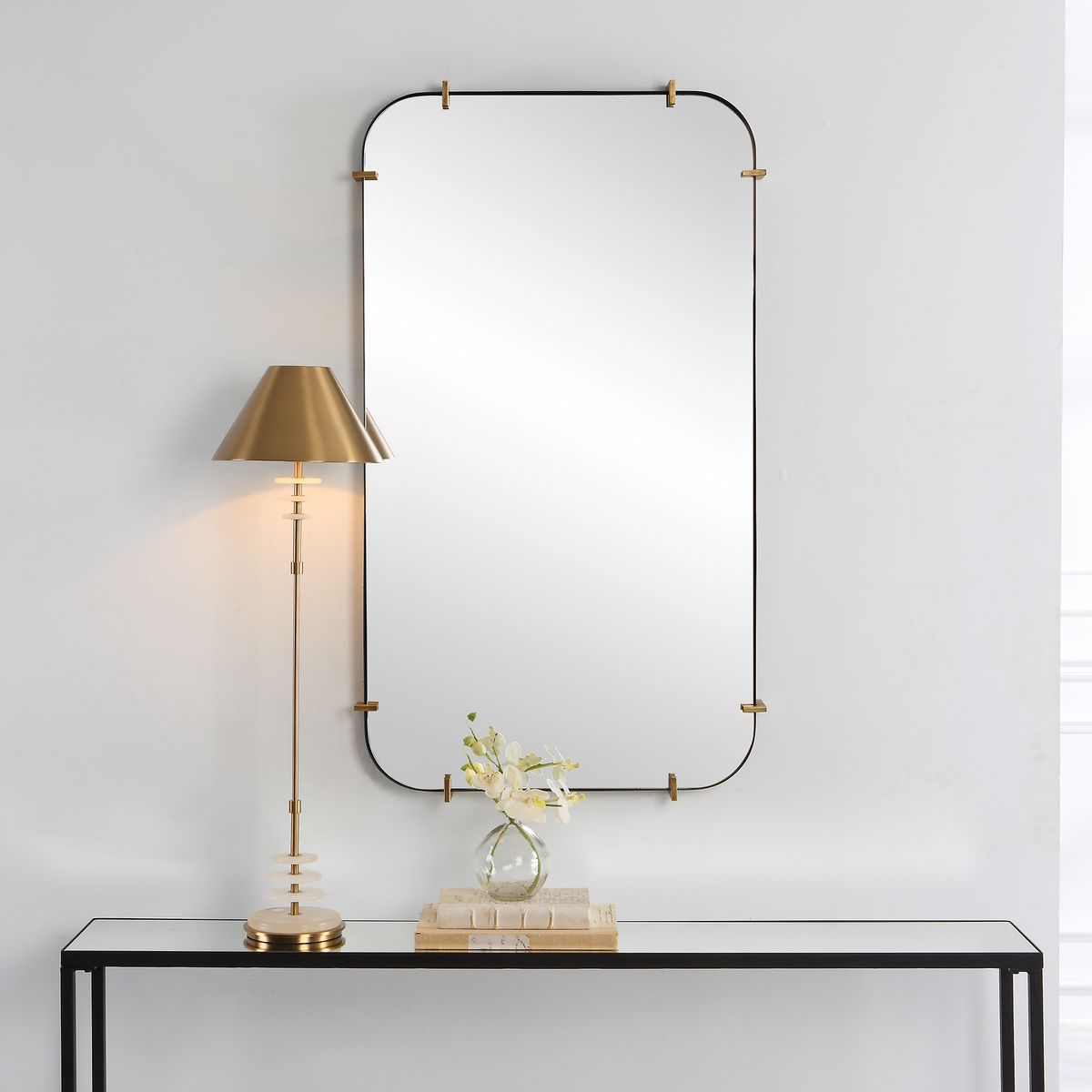 Decorative mirror with gold frame and lamp on a console table against a white wall.