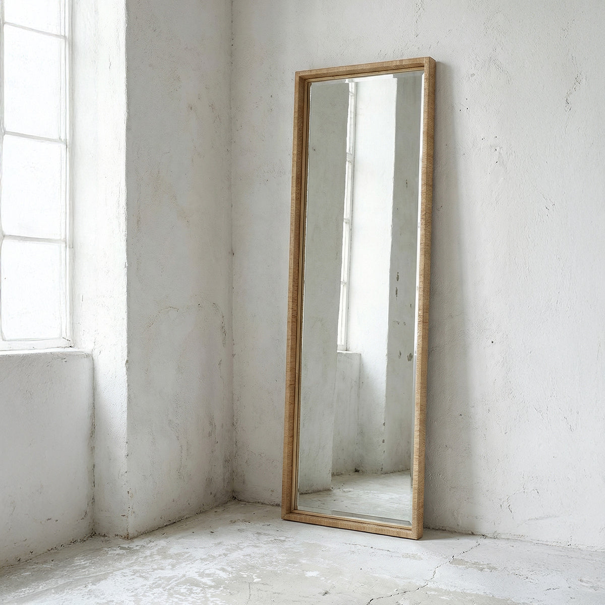 Full-length rattan mirror with frame leaning against a white wall.