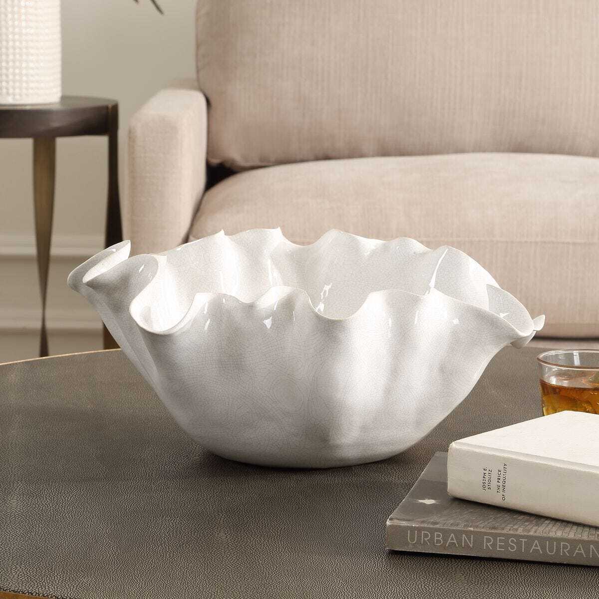 White decorative bowl on a coffee table with a book and glass in a living room setting